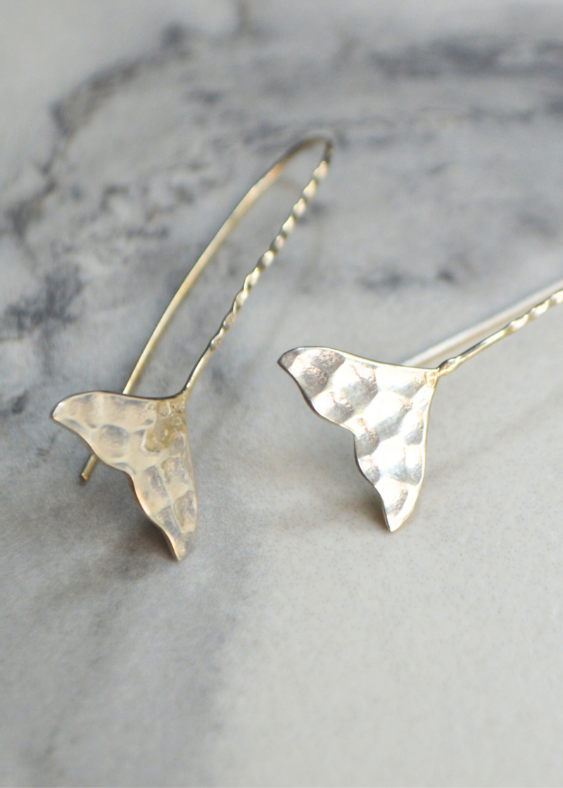 close up of 925 sterling silver whale tail earrings with long fish hook placed on a white marble background