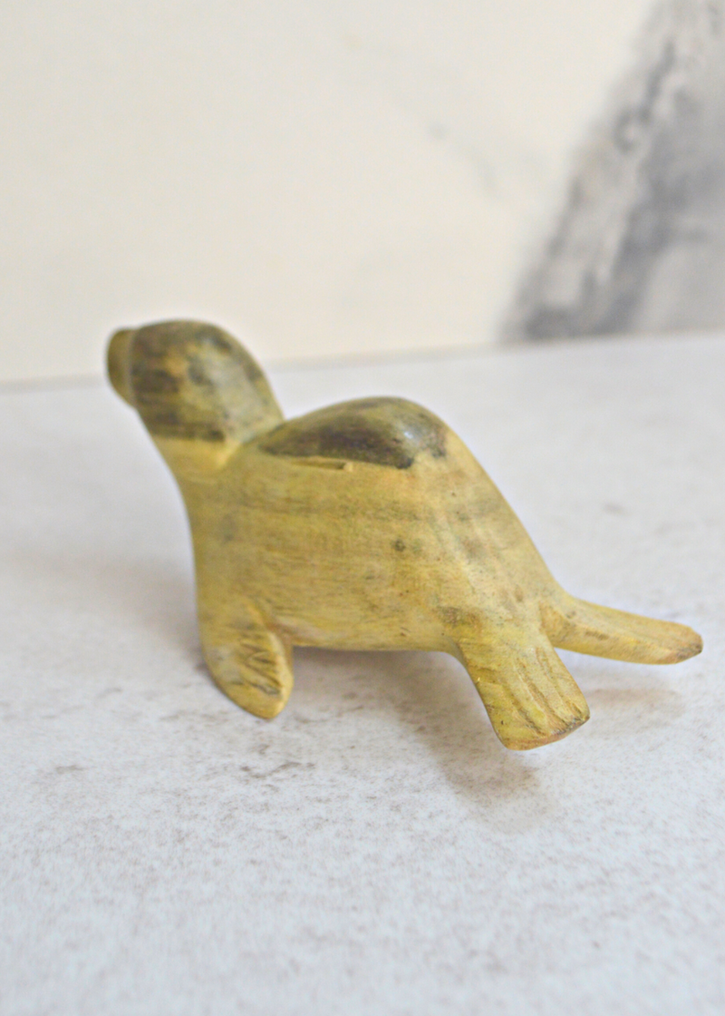 a small green and yellow wooden seal decoration from a side view on a white surface and marble background