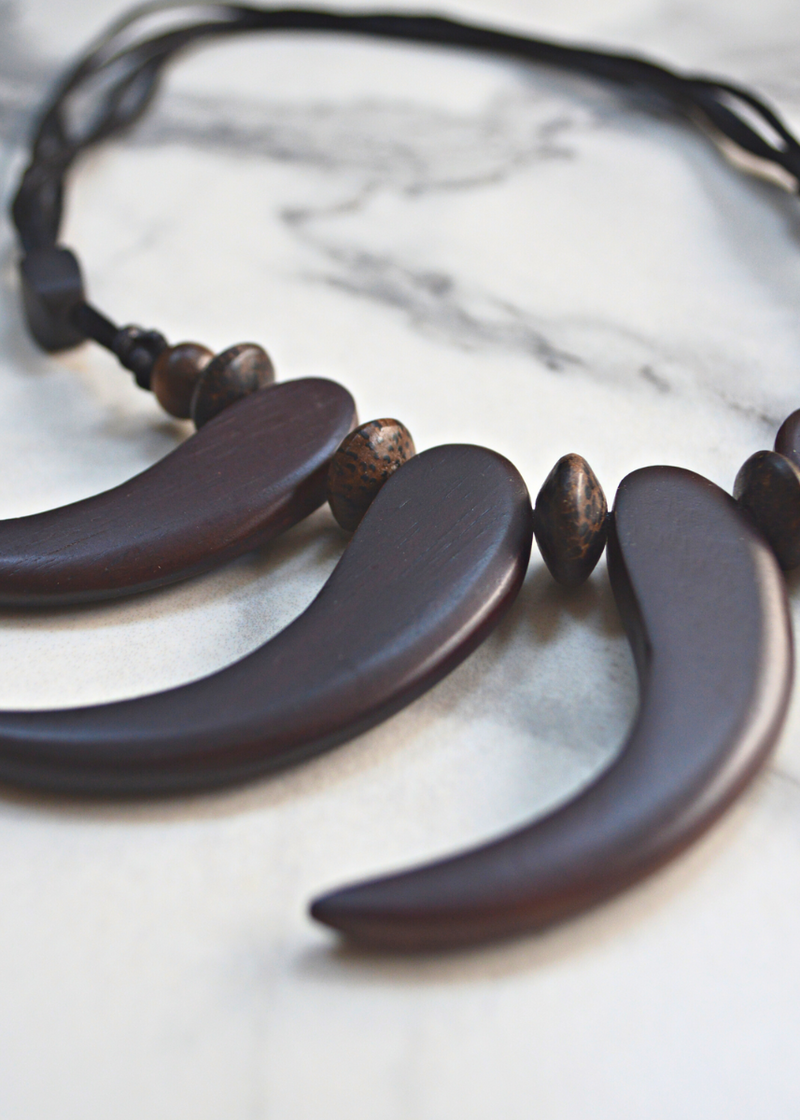 close up of brown wooden tribal necklace with beads laid on a marble surface