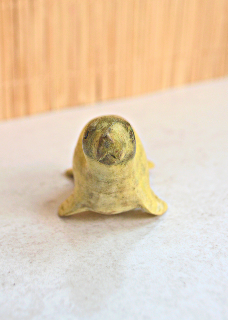 front of a small green and yellow wooden seal decoration on a white surface
