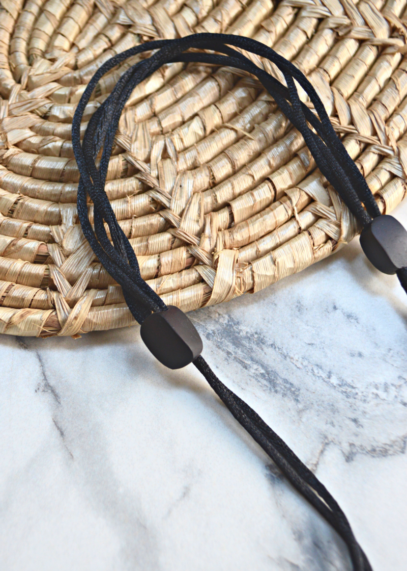 close up of adjustable straps of a brown wooden tribal necklace with beads laid on a marble surface and woven matt