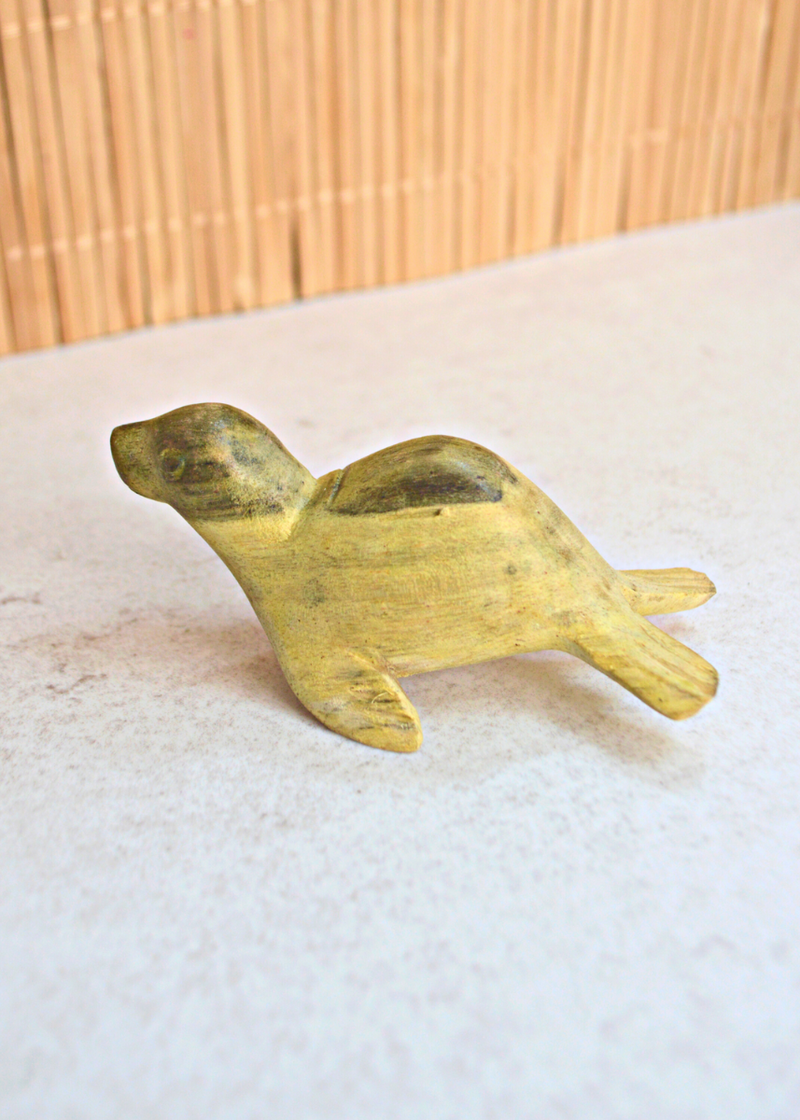 a small green and yellow wooden seal decoration from a side view on a white surface