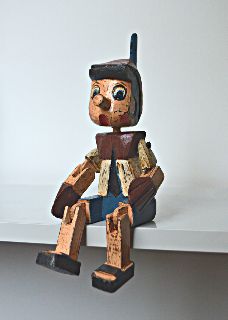 Shabby chic wooden pinnochio shelf sitter sat on a white shelf with a white background