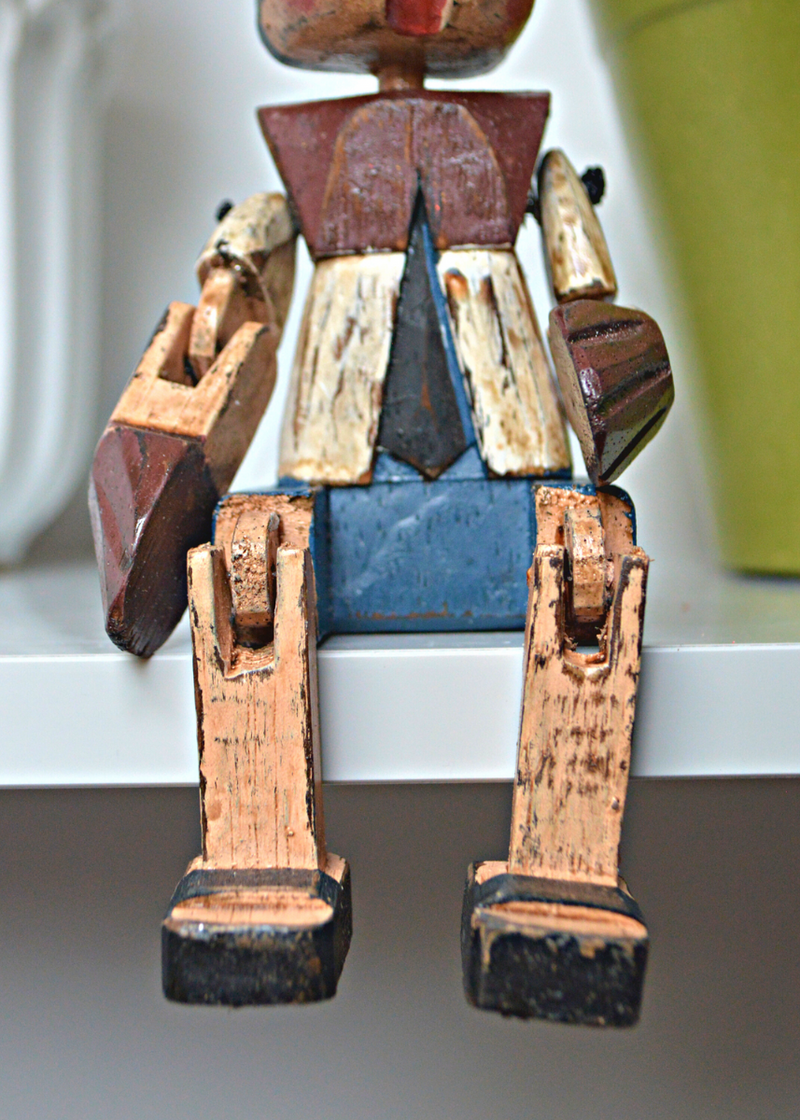 close up of Shabby chic wooden pinnochio shelf sitter legs and body sat on a white shelf with plant pots in the background