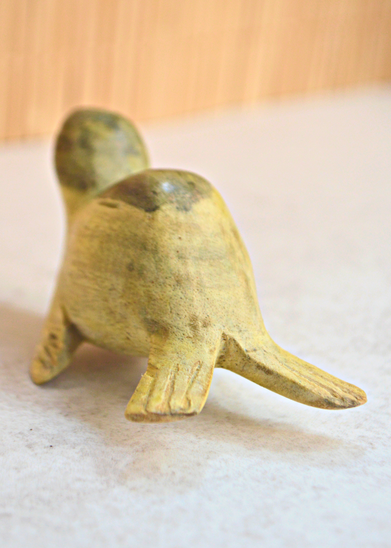 back of a small green and yellow wooden seal decoration on a white surface