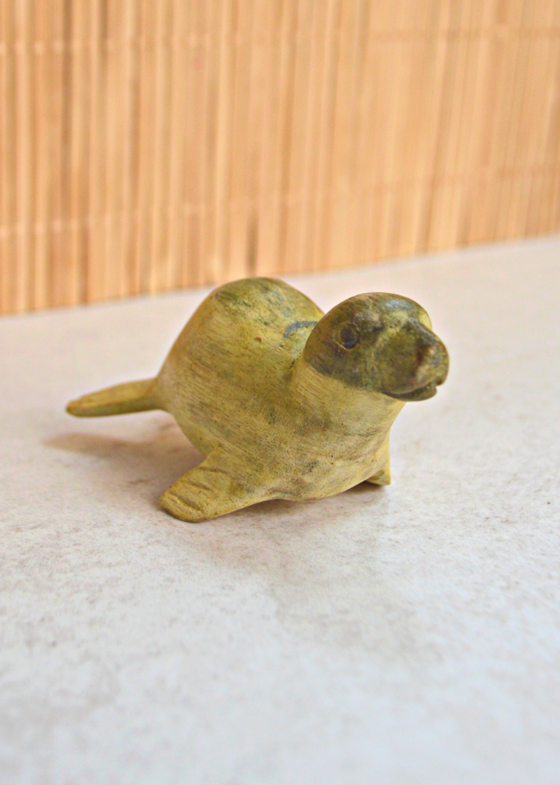 close up of a small green and yellow wooden seal decoration from a front side angle laid on a white surface