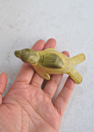 small green and yellow wooden seal decoration laid on someones hand from birds eye view