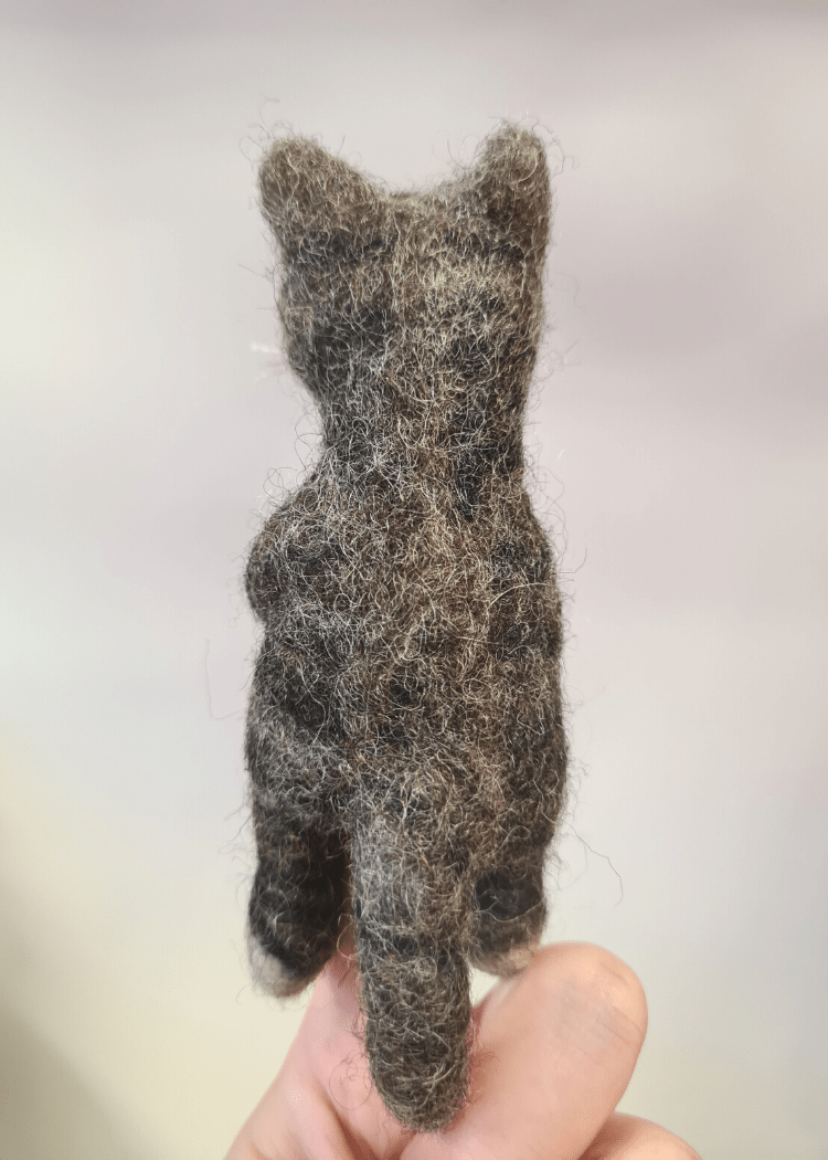 the back of a grey stripy felt cat finger puppet someones finger