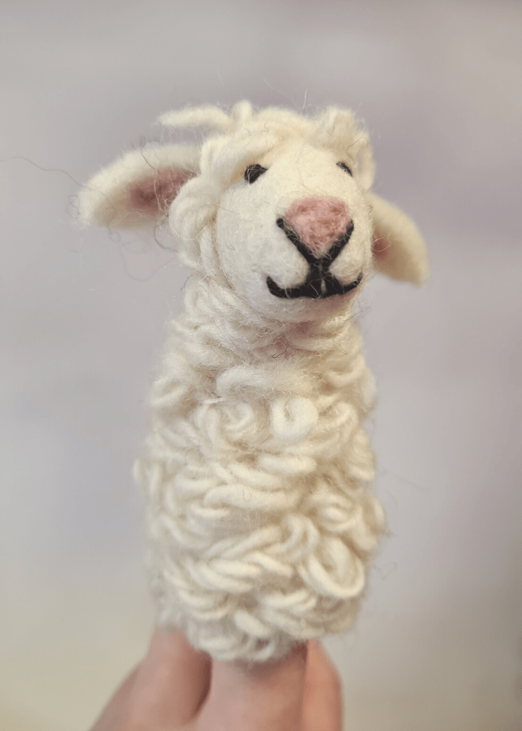 white felt sheep finger puppet with pink nose and black thread smile and eyes sat on someone&