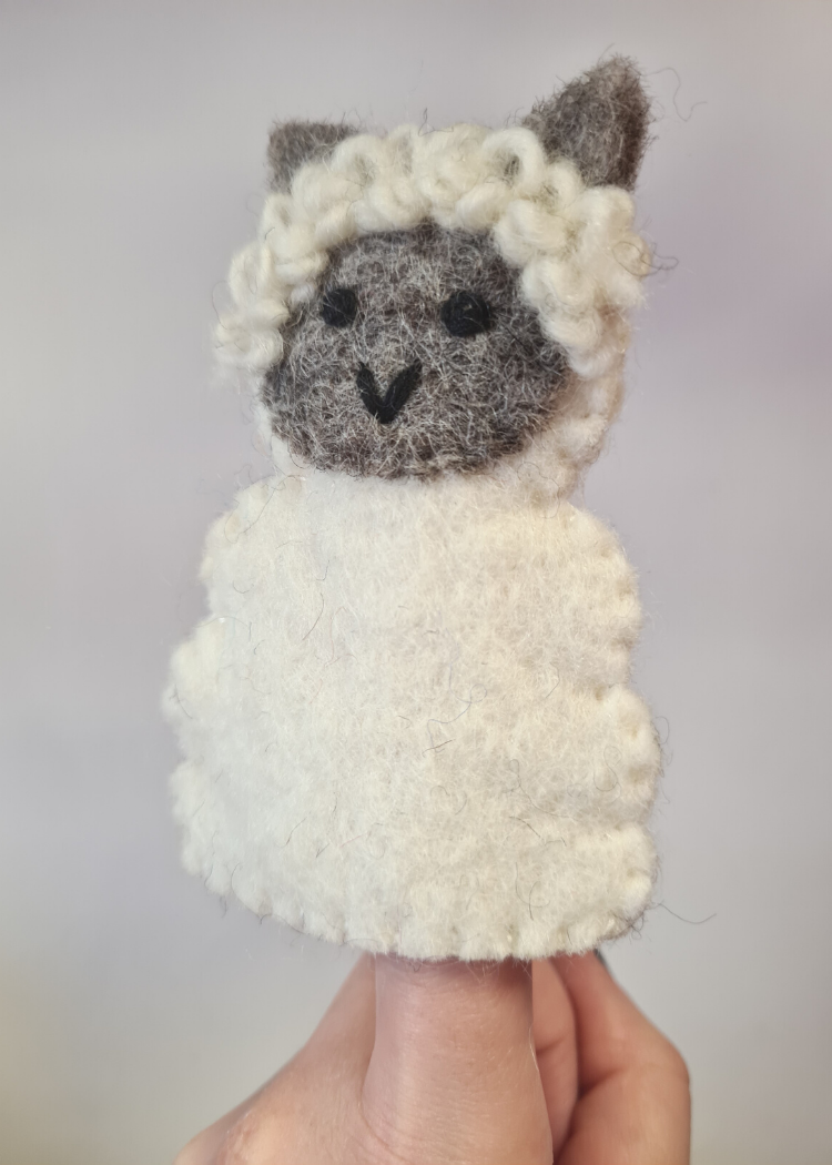 felt white sheep finger puppet with cute grey face and ears sat on someones finger