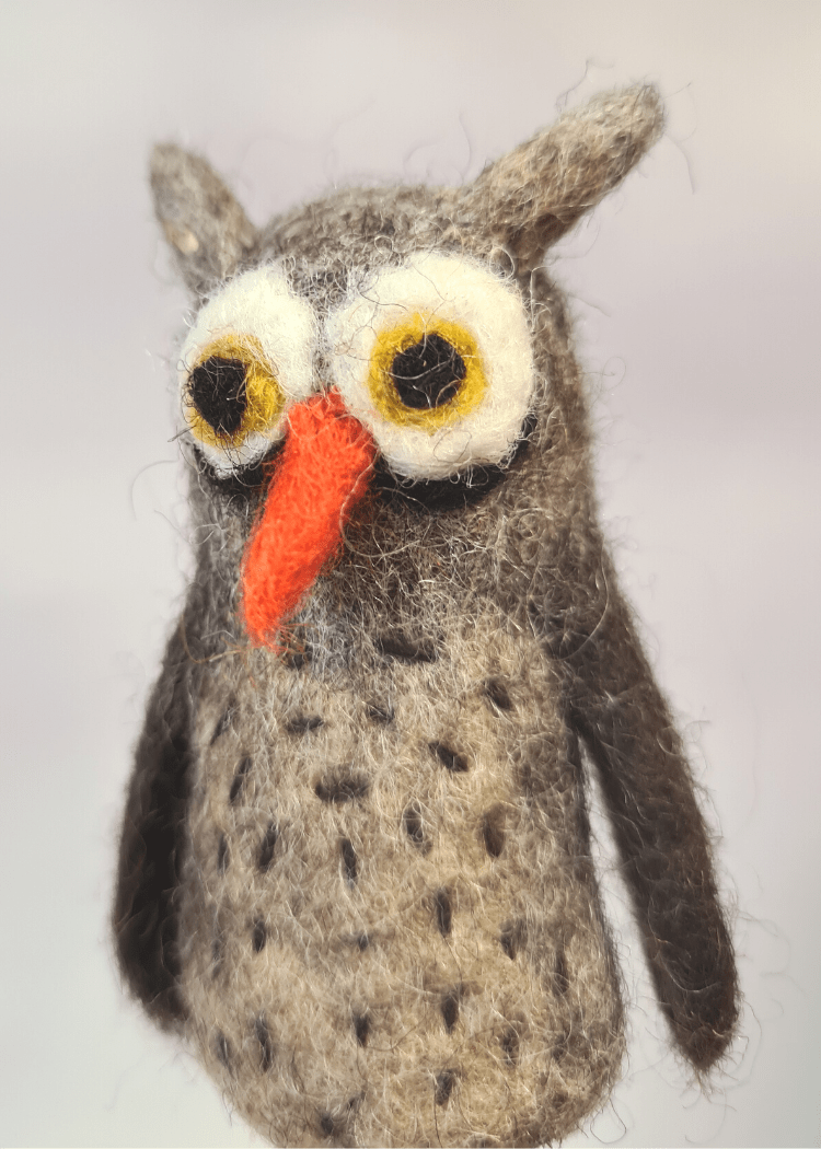 close up of a brown felt owl finger puppet with orange nose and big white and brown eyes