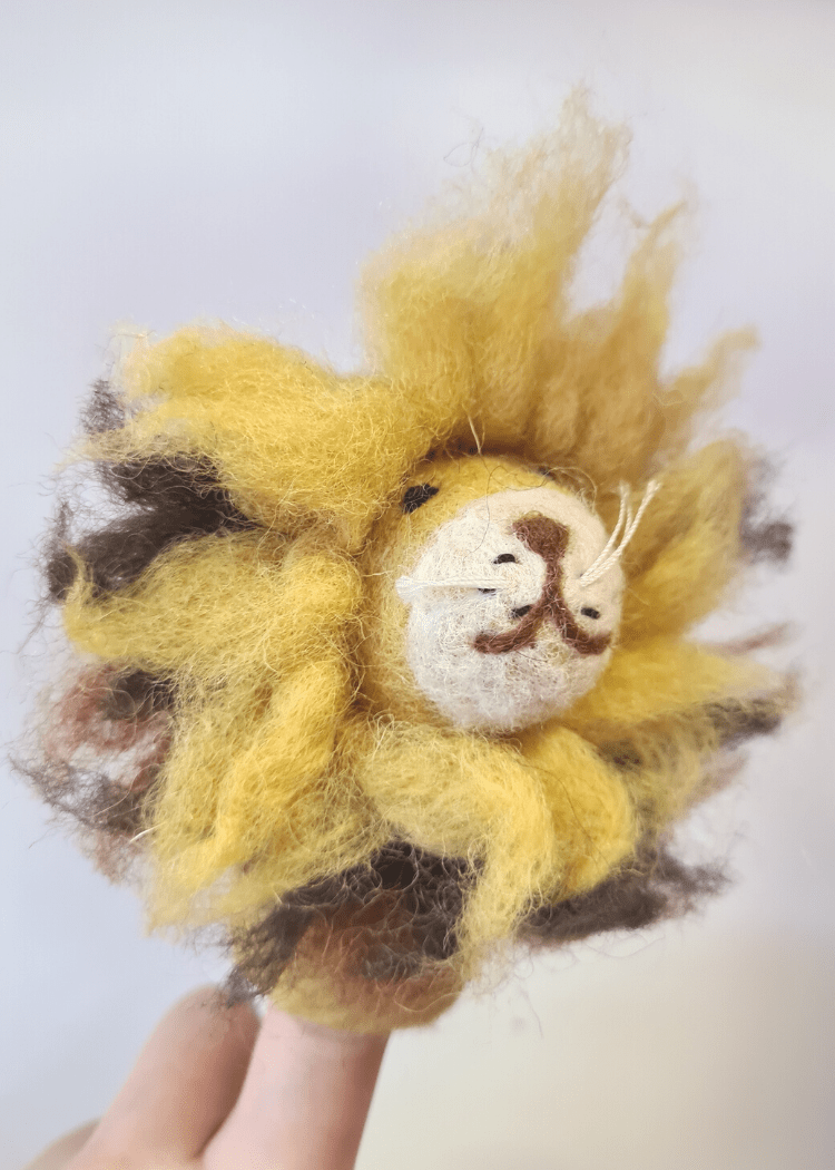 side close up of a wild yellow felt lion with smiley brown face and fuzzy mane sat on someone&