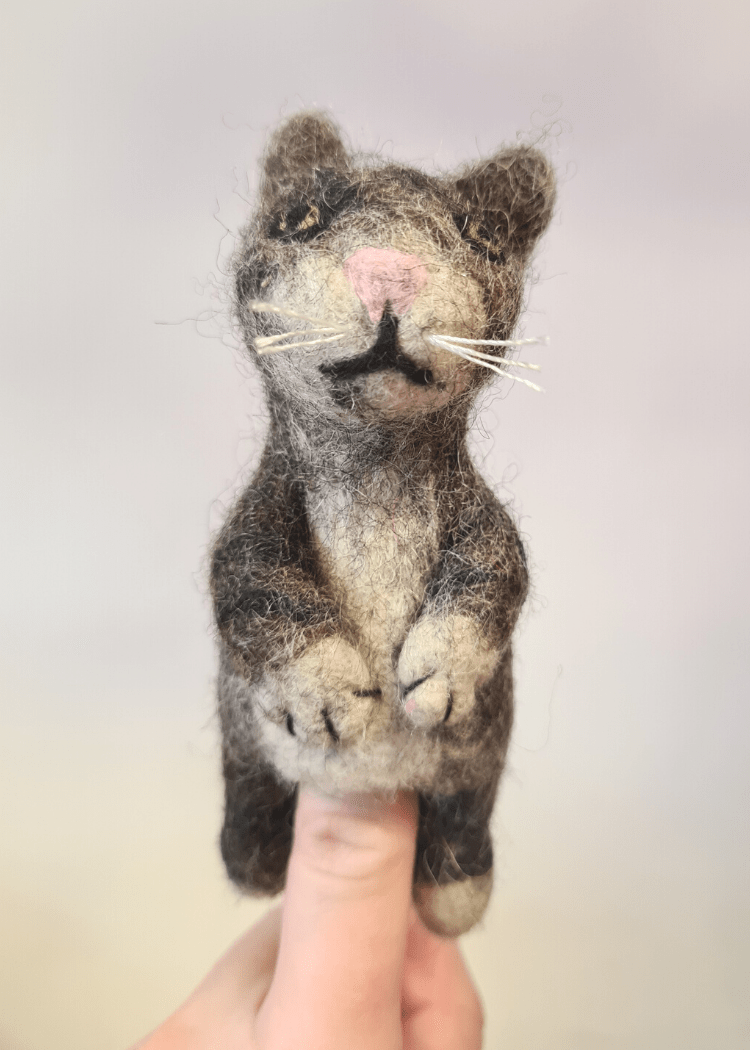 grey stripy felt cat finger puppet with white whiskers and pink nose sat on someones finger