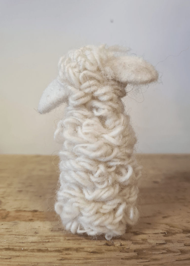 back of white felt sheep finger puppet sat on a wooden top
