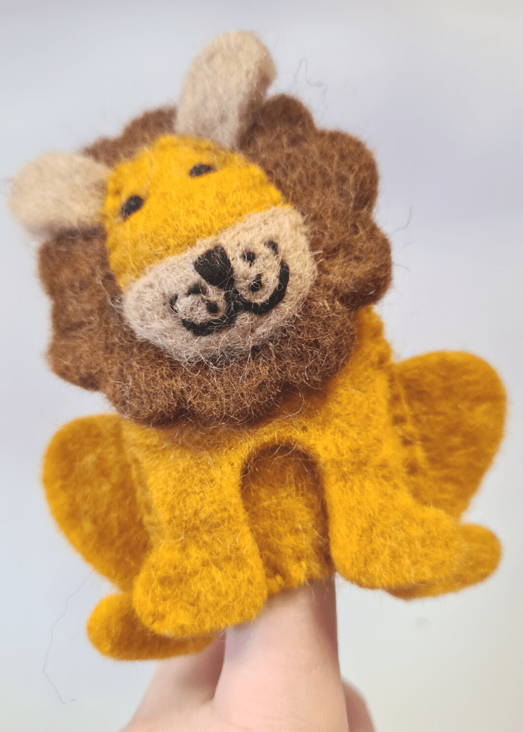 close up of a sitting felt yellow lion finger puppet with brown mane and smiley face sat on someone&