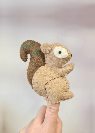 light brown felt squirrel finger puppet with dark brown tail and leaves on, sat on someones finger
