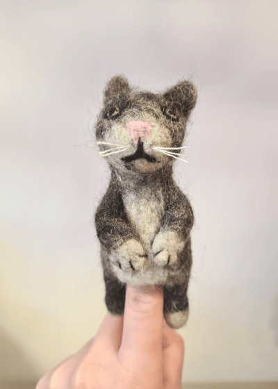 grey stripy felt cat finger puppet with white whiskers and pink nose sat on someones finger