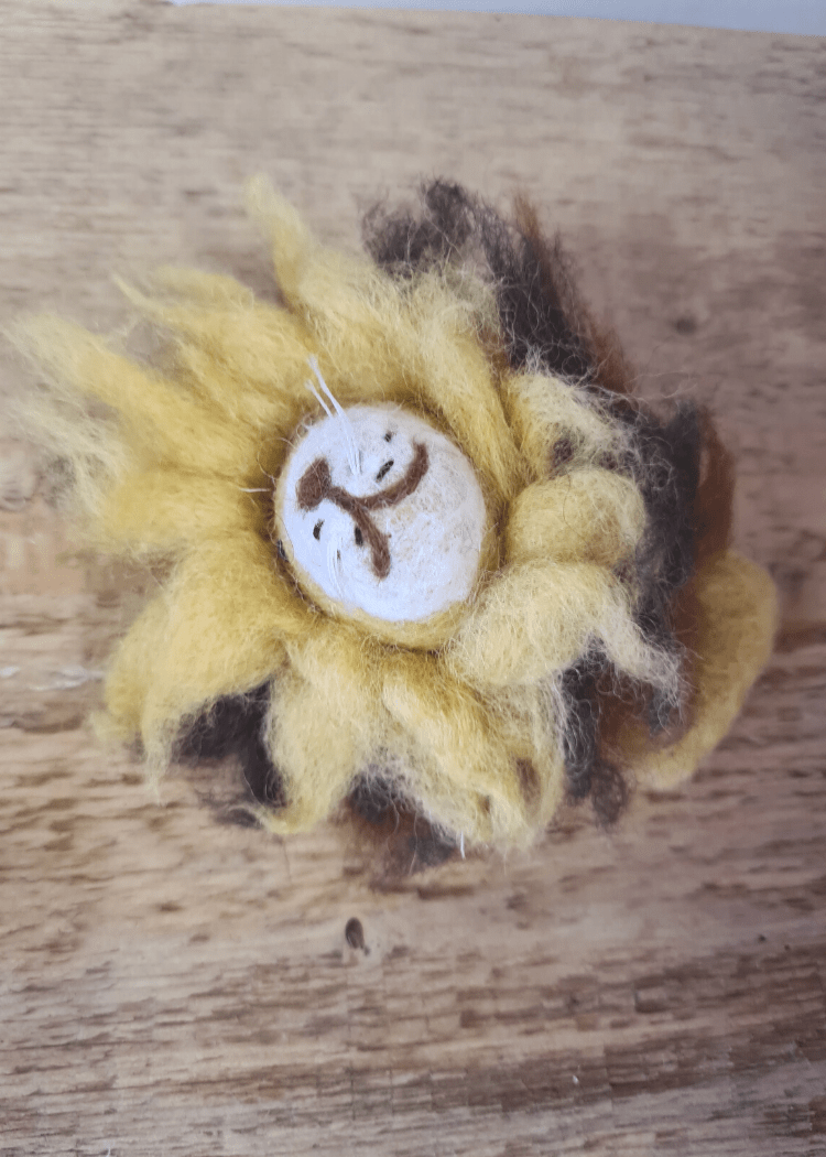 wild yellow felt lion with smiley brown face and fuzzy mane laying on a wooden surface