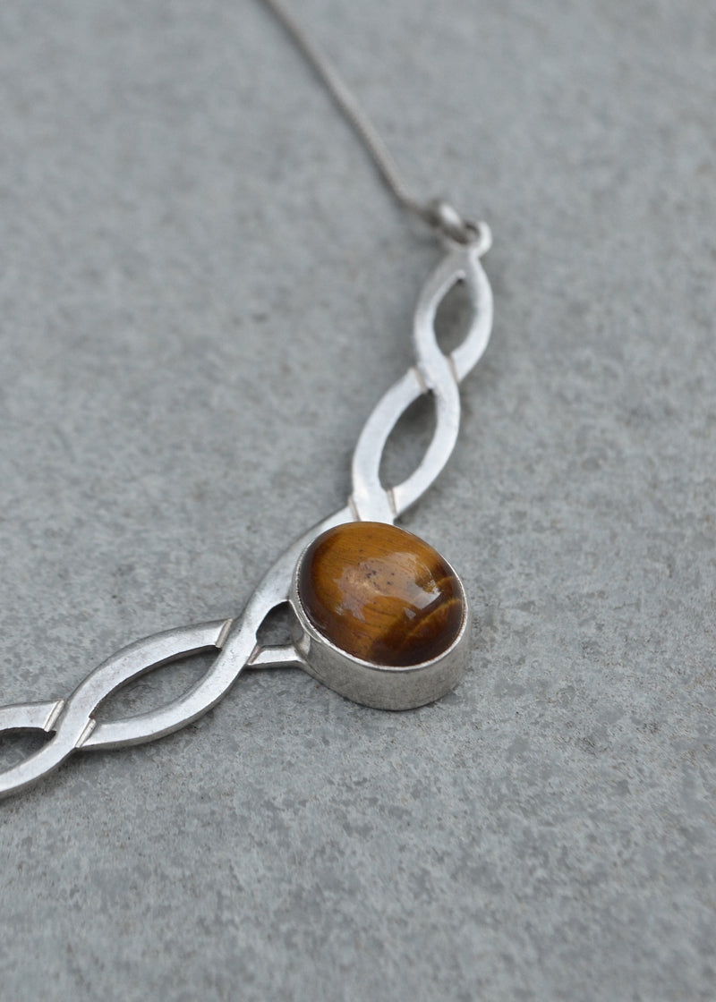 silver celtic twist necklace with tigers eye stone resting on a grey surface