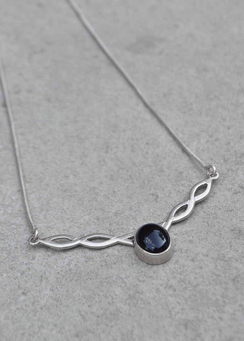 silver celtic twist necklace with black onyx stone resting on a grey surface