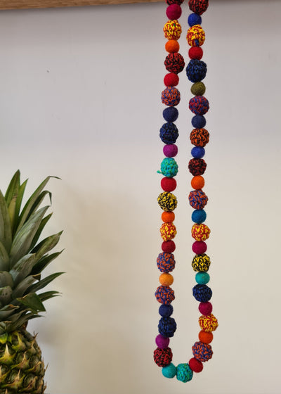 Large Felt Multi Colour Pom Pom Necklace hanging next to pineapple