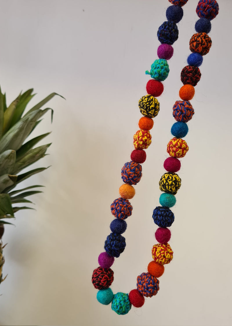 Large Felt Multi Colour Pom Pom Necklace hanging on an angle next to pineapple