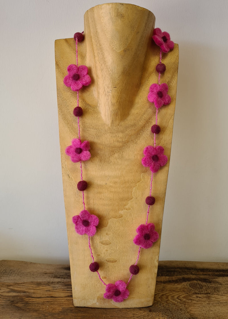 Pink pom pom flower necklace with beads sat on a wooden neck mannequin