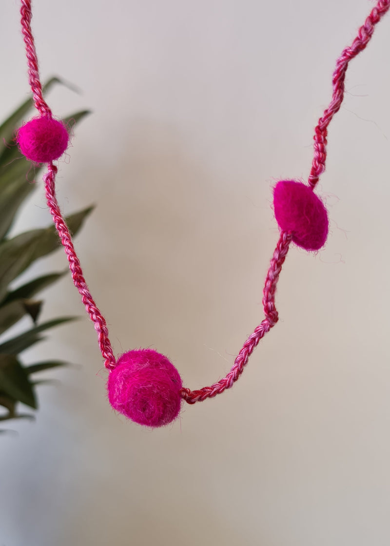 close up of Pink Pom Pom Felt Necklace with blurred pineapple in the background