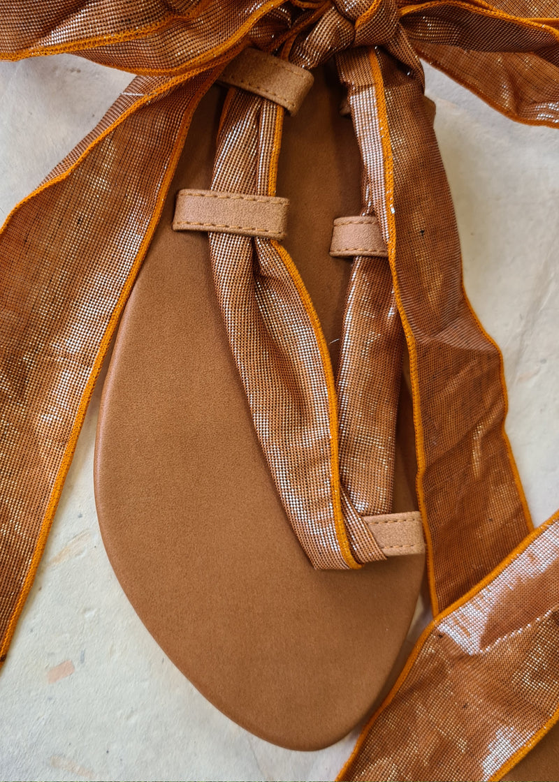 close up of brown metallic lace up sandal tied in a bow at the back