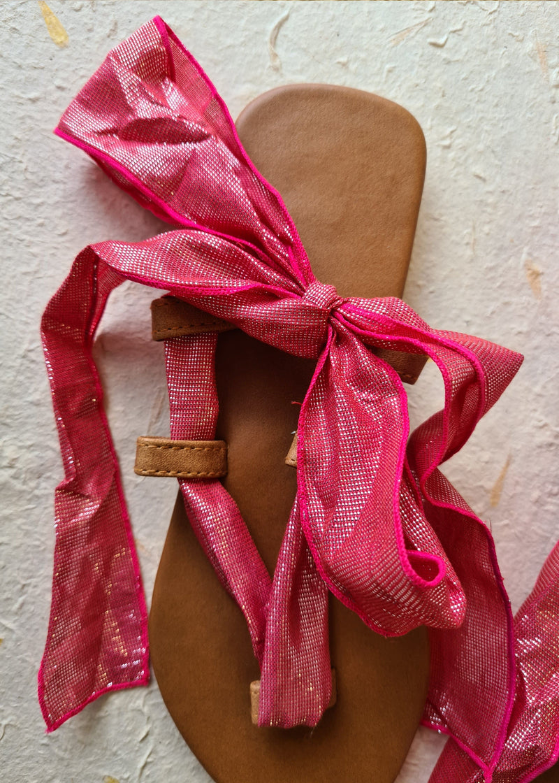close up of pink metallic lace up sandals tied in a bow