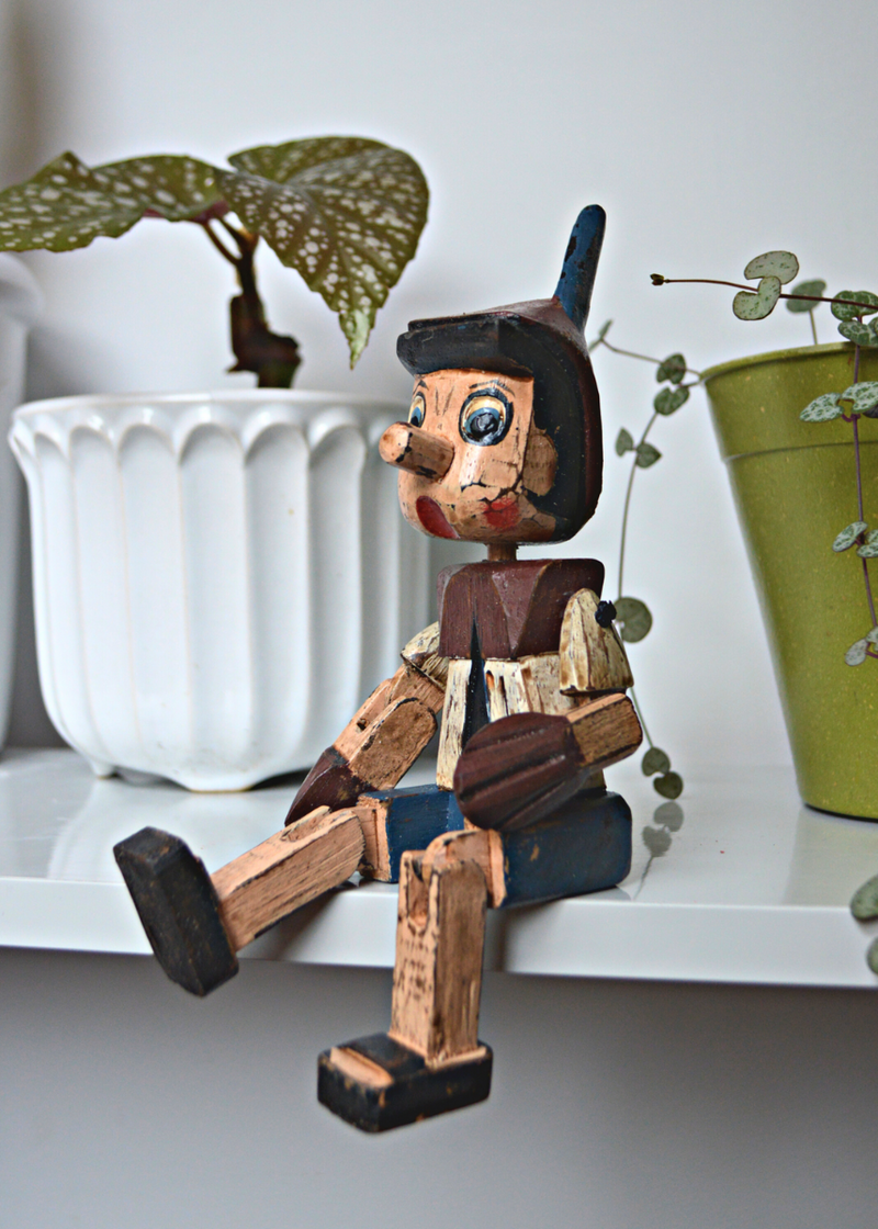 Shabby chic wooden pinnochio shelf sitter sat on a white shelf with plants in the background