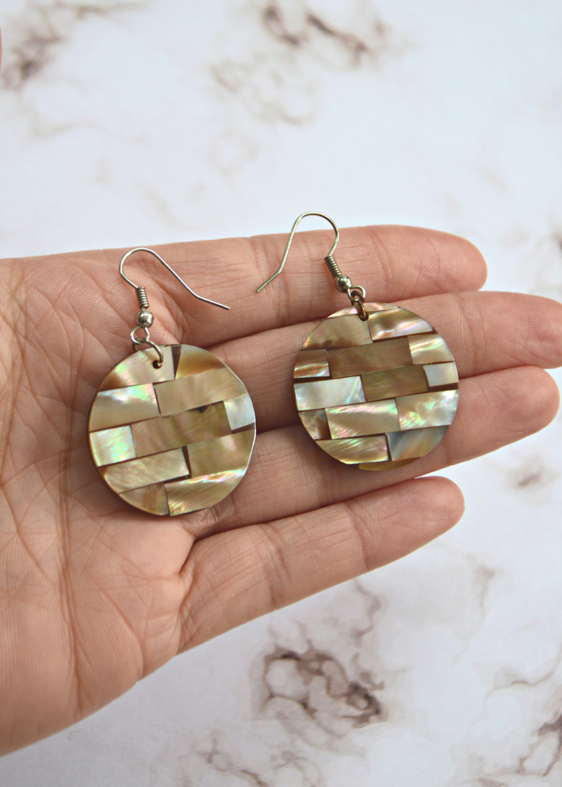 light brown Mother of Pearl Disc Earrings laid on someones hand in front of a marble textured background