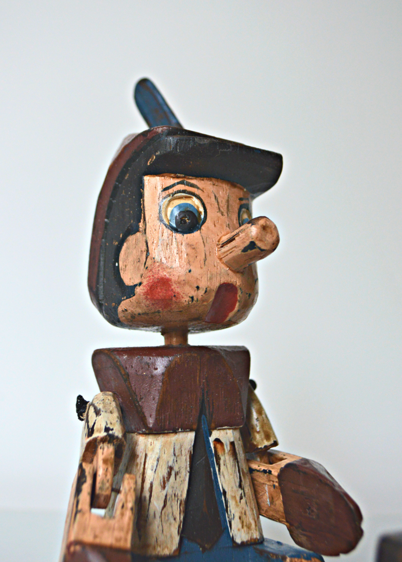 close up of Shabby chic wooden pinnochio shelf sitter face and body sat on a white shelf with white background