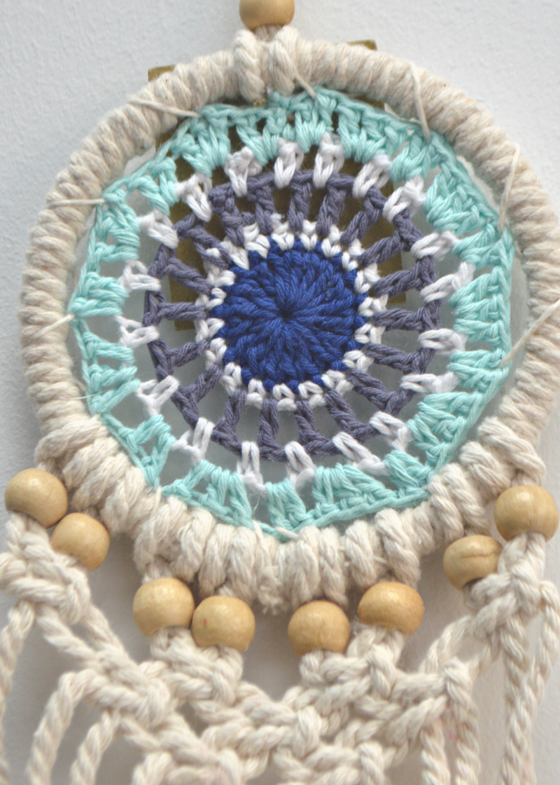 close up of a white dreamcatcher with different shades of blue crocheted in the centre and white threads with wooden beads on the bottom