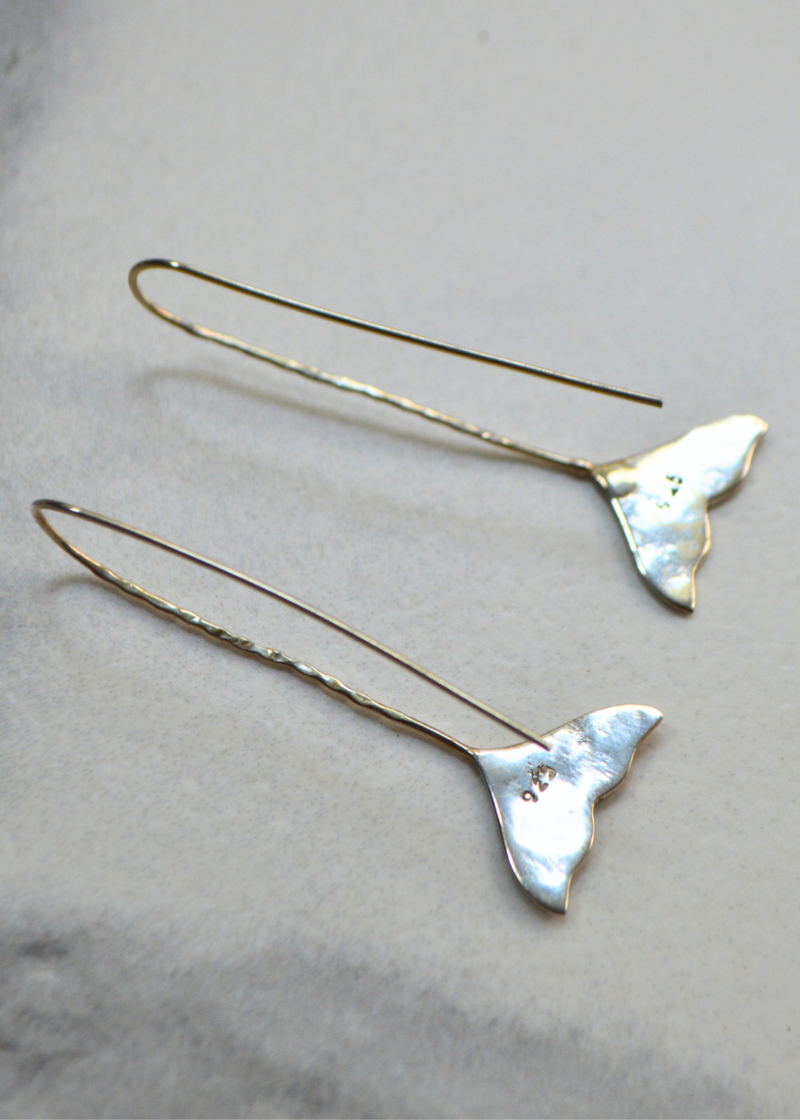 the back of a pair of 925 sterling silver whale tail earrings with long fish hook placed on a white marble background