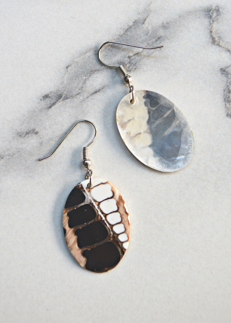two brown and white Oval Shell Earrings With Fossil Detail and ear wires laid on a marble surface, one showing the front and the other showing the back
