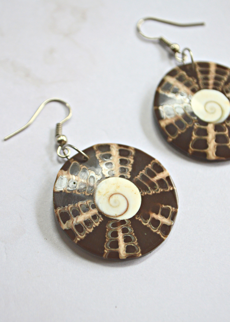 close up of Dangle drop earrings with white shiva eye shell in the centre and brown pattern surrounding it laid on a white surface