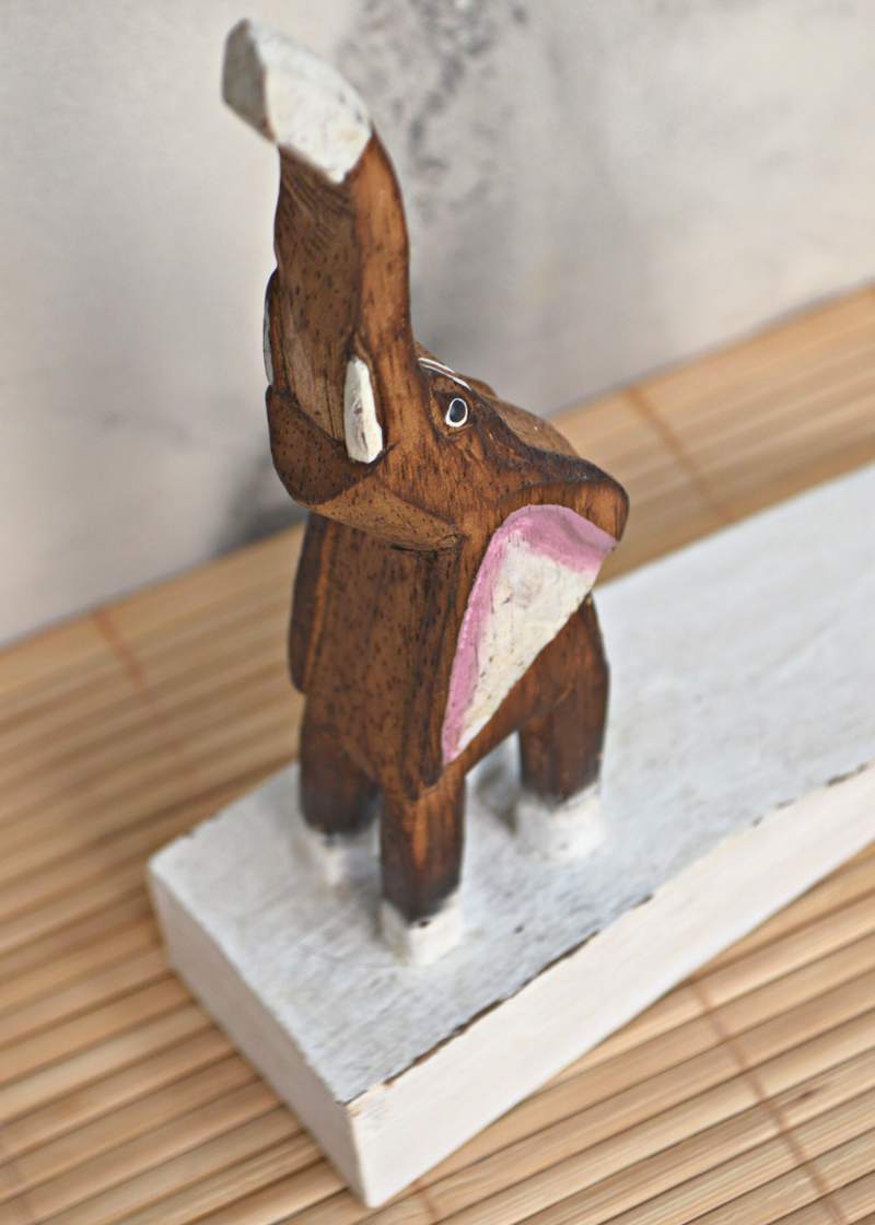 close up of a wooden brown and white elephant door stop with pink detail on ears, stood on a bamboo matt with marble background
