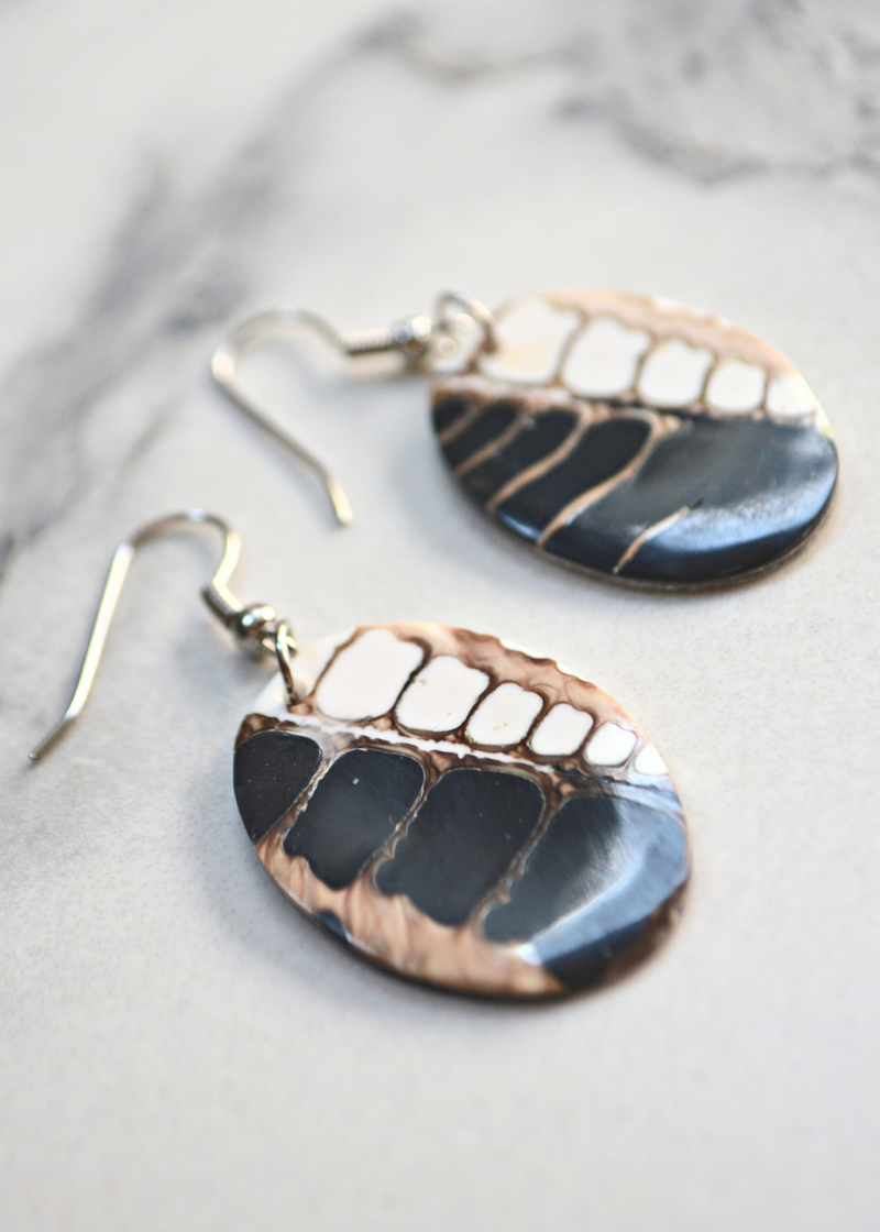 close up of brown and white Oval Shell Earrings With Fossil Detail with ear wires laid on a marble surface