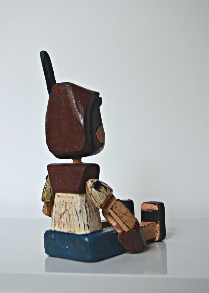 the back of a Shabby chic wooden pinnochio shelf sitter sat on a white shelf with white background
