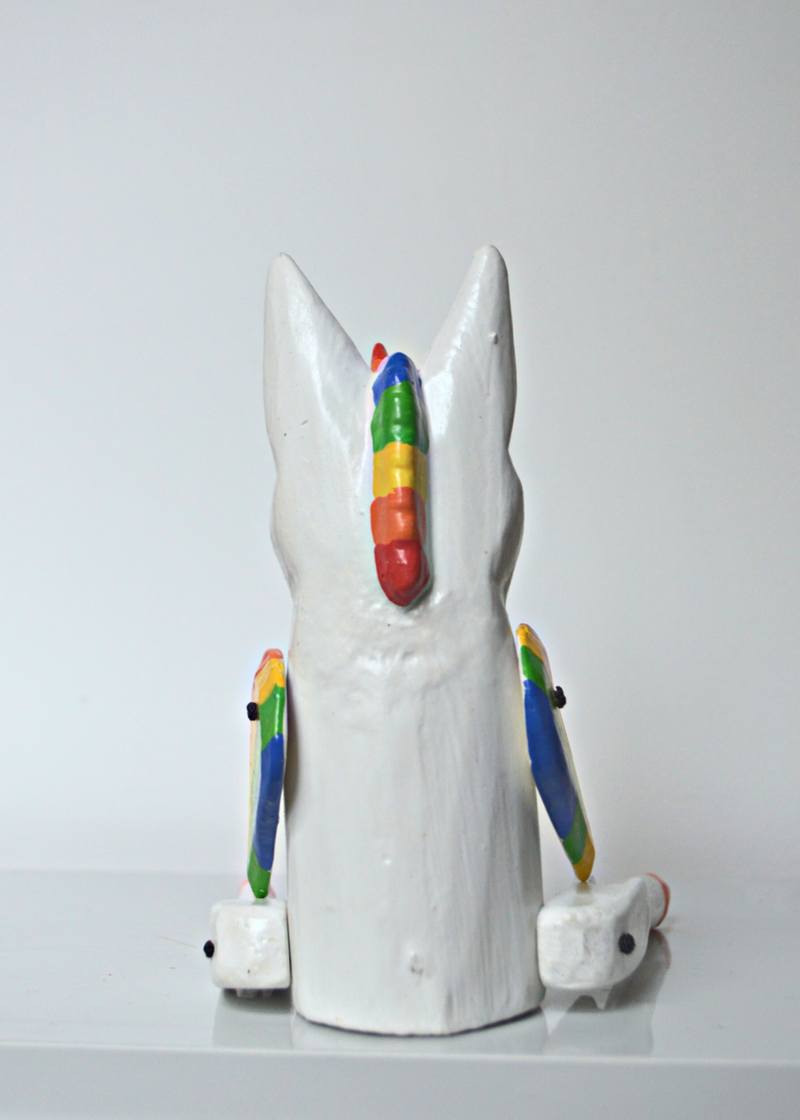 back of white and pink wooden unicorn with rainbow horn and wings sat on a white wooden shelf in front of white background