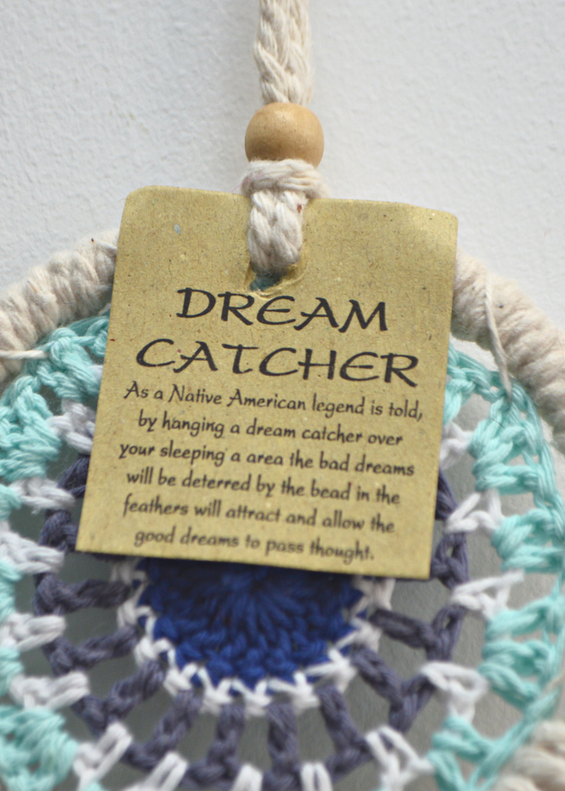 a white dreamcatcher with different shades of blue crocheted in the centre with wooden beads and a label attached hanging in front of a white background