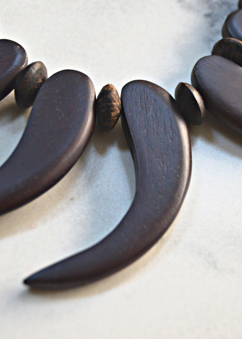 close up of a brown wooden tribal necklace with beads laid on a marble surface