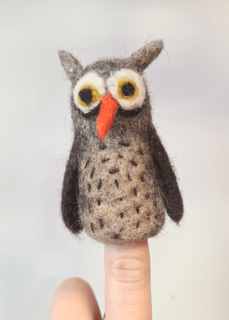 brown felt owl finger puppet with orange nose and big white and brown eyes sat on someone&