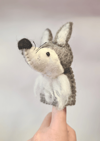 felt grey and white wolf finger puppet with black nose, whiskers and bead eyes sat on someone's finger