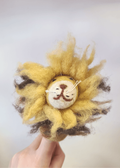 wild yellow felt lion with smiley brown face and fuzzy mane sat on someone's finger