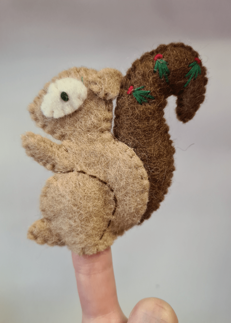 light brown felt squirrel finger puppet with dark brown tail and leaves on, sat on someones finger