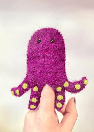 purple felt octopus finger puppet with yellow spots and smiley face with beads on someones finger