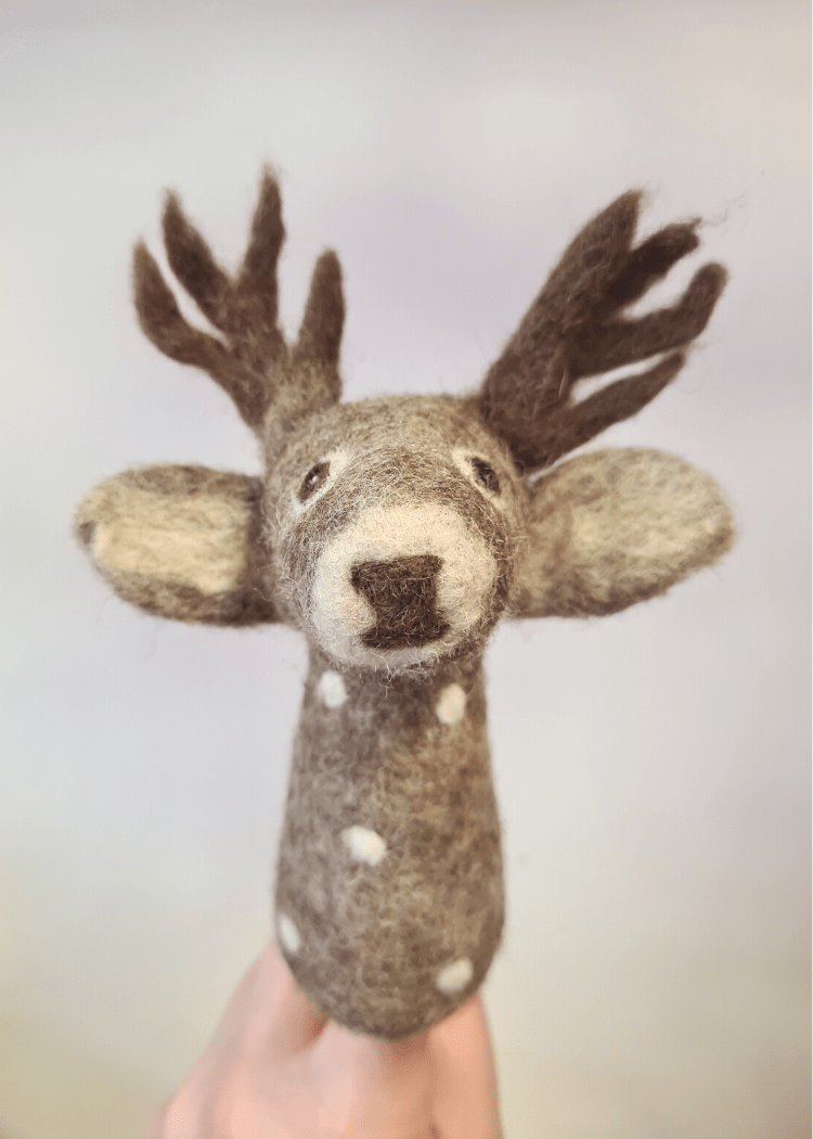 grey felt deer finger puppet with white spots, brown antlers and nose, a cute face and big ears sat on someones finger