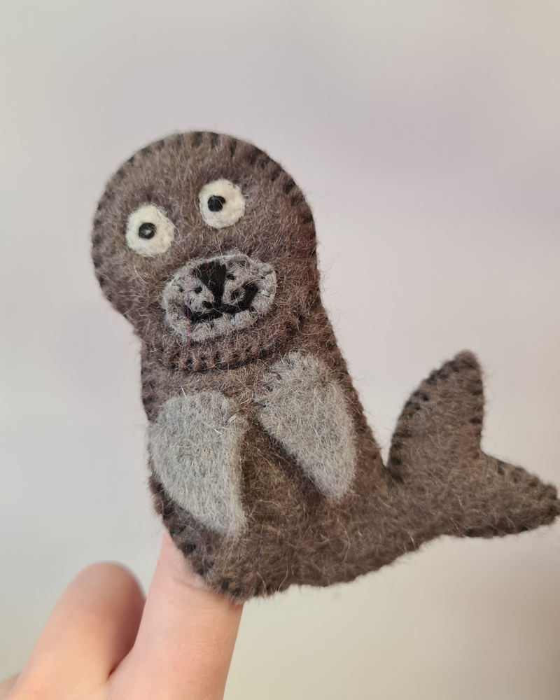 Dark grey felt seal finger puppet with a sewn on smiley face on someones finger